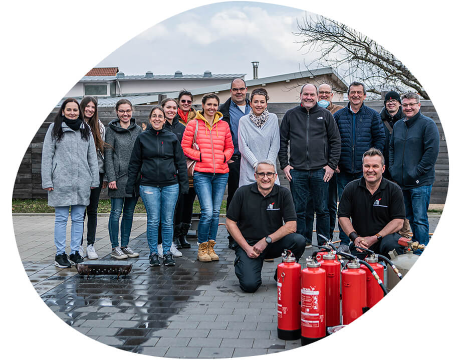 Ein Bild von zufriedenen Teilnehmern mit unseren Partner-Dozenten und Feuerlöschern im Vordergrund